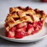 Close-up of a juicy slice of strawberry rhubarb pie showing the filling and golden lattice crust.