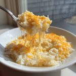A spoonful of creamy, cheesy rice showing long, dramatic cheese pulls, highlighting the texture of the cheesy rice.