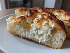 Close-up of a thick slice of white pizza showing the fluffy crust and generous layer of creamy, melted cheese topping.