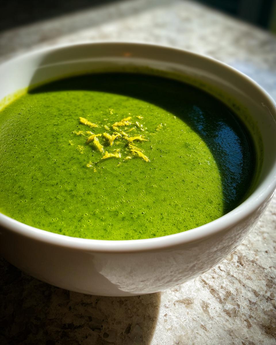 Close-up of a bowl of bright green asparagus soup topped with yellow lemon zest.