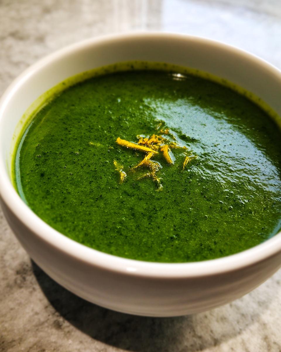 Close-up of a bowl of vibrant green asparagus soup garnished with yellow zest.