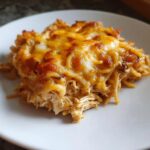 Close-up of a serving of cheesy chicken spaghetti, showing shredded chicken and melted, browned cheese topping.