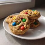 A stack of freshly baked, chewy m&m cookies studded with colorful candies, resting on a white plate.