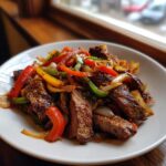 A white plate piled high with colorful steak fajita strips, sautéed onions, and bell peppers.