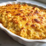 Close-up of a hot, baked crab dip topped with melted, browned cheddar cheese in a white dish.