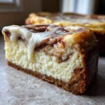 Close-up of a thick slice of cinnamon roll cheesecake, showing the creamy filling, cinnamon swirl, and white icing drizzle.
