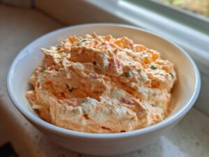 Close-up of creamy, orange-colored boat dip mixture served in a white bowl near a window.