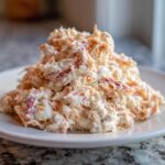 A mound of creamy, shredded seafood salad with visible pink/orange pieces, served on a white plate.