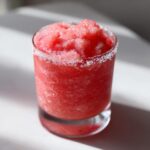 Close-up of a vibrant, icy strawberry daiquiri in a glass with a sugared rim.