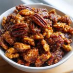 Close-up of a white bowl filled with glistening, caramelized pecans and walnuts, showcasing the texture of the praline crunch.