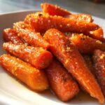 A close-up shot of bright orange, tender honey glazed carrots coated in a shiny glaze and sprinkled with herbs.