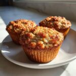 Three golden brown banana oatmeal muffins with a crumbly top sitting on a white plate.