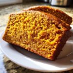 Close-up of two moist slices of easy pumpkin bread with a vibrant orange crumb, sitting on a white plate.