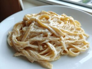 Close-up of fettuccine pasta generously coated in creamy olive garden alfredo sauce, seasoned with pepper.
