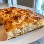 Close-up of a golden-brown slice of fluffy cottage cheese bread on a white plate.