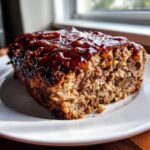 A thick slice of moist stove top stuffing meatloaf topped with a shiny, dark glaze on a white plate.