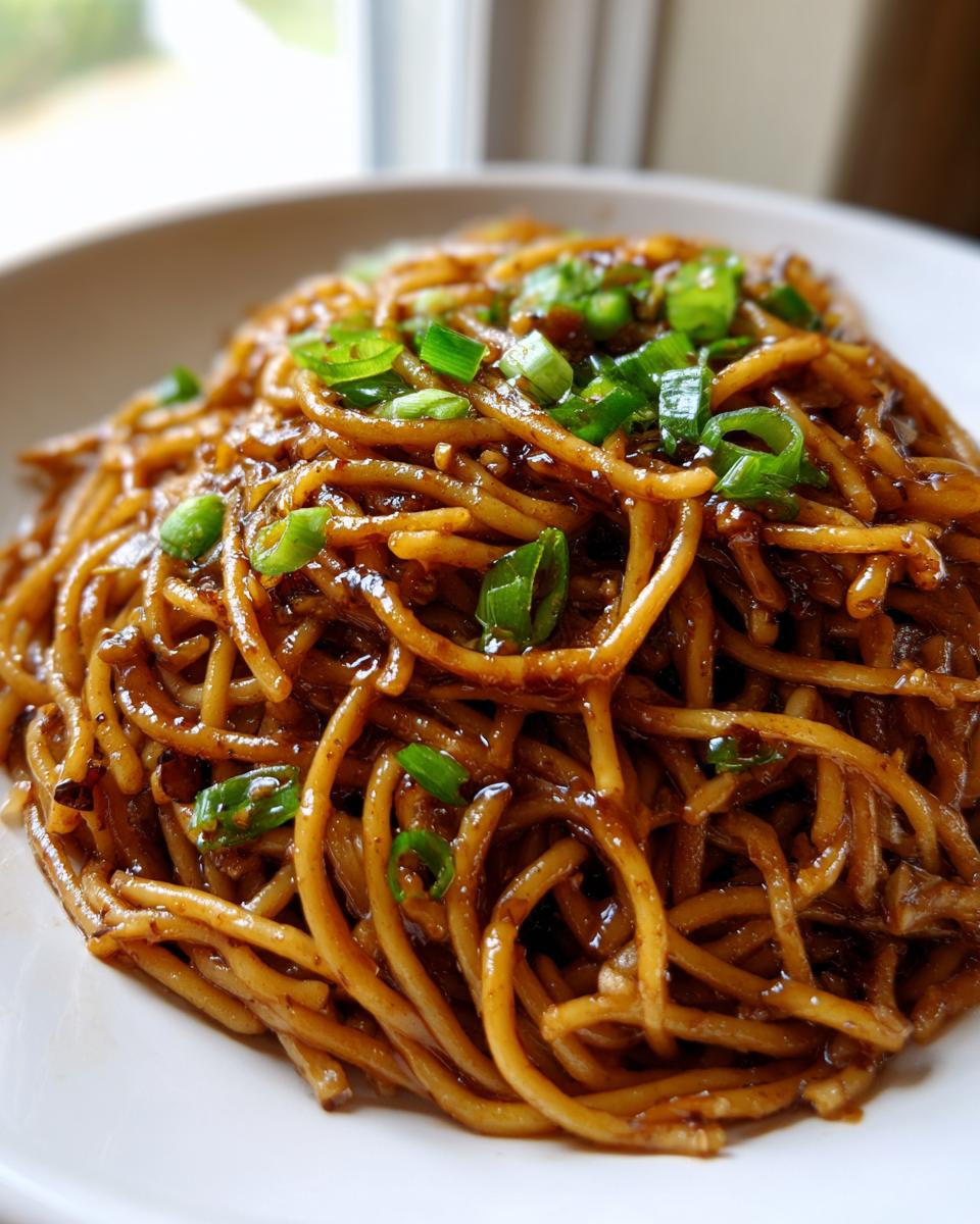 A close-up shot of a serving of rich, dark brown garlic noodles topped generously with fresh chopped green onions.