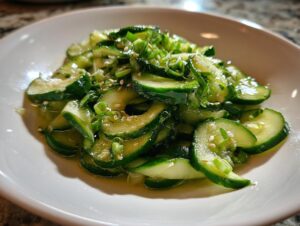 Close-up of vibrant, sliced cucumbers in a glossy dressing, garnished with sesame seeds and green onions, showcasing the asian cucumber salad.