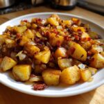 A close-up of golden-brown, cubed Bacon and Onion Skillet Potatoes served on a white plate.