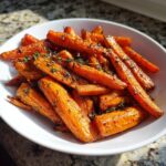 A white bowl filled with glossy, caramelized Balsamic Roasted Carrots garnished with fresh thyme sprigs.