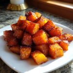 A pile of glistening, caramelized cubes of Brown Sugar Roasted Butternut Squash on a white plate.