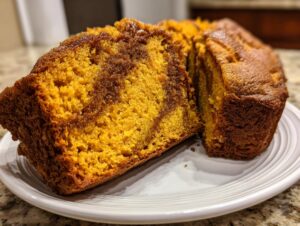 A close-up view of a sliced loaf of vibrant orange Cinnamon Swirl Pumpkin Bread showing the rich brown cinnamon swirl pattern.