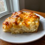 A square serving of Cream Cheese Chicken Bake with a bubbly, golden-brown melted cheddar cheese topping on a white plate.