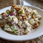 Close-up of creamy Baked Marinated Chicken Salad mixed with red onion, celery, and topped with walnuts.