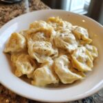 Close-up of cheesy tortellini covered in creamy sauce, seasoned with black pepper, for a Tortellini Alfredo Recipe.
