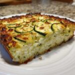 A close-up of a serving of Garlic Parmesan Zucchini Casserole with a golden-brown, cheesy top and visible zucchini slices.