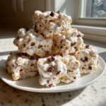 A stack of homemade avalanche cookies coated in white chocolate and mixed with chocolate chips, sitting on a white plate.