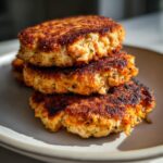 Close-up of three perfectly pan-fried Homemade Salmon Patties stacked on a light gray plate.