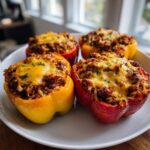 Four colorful Keto Stuffed Bell Peppers, filled with meat and topped with melted cheddar cheese, served on a white plate.
