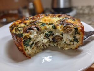 Close-up of a single serving of Low-Carb Chicken Spinach Mushroom Casserole with a bite taken out, showing shredded chicken, spinach, and mushrooms.