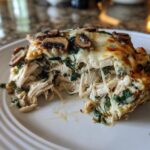 A cheesy, pulled slice of Low-Carb Chicken Spinach Mushroom Casserole showing shredded chicken and melted cheese strings.