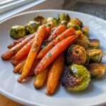 A close-up of roasted Maple Glazed Carrots and Brussels Sprouts glistening on a white plate.
