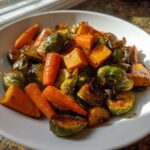 A close-up of glistening Maple Roasted Thanksgiving Veggies featuring caramelized Brussels sprouts, carrots, and cubed squash in a white bowl.
