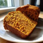 Close-up of two thick slices of moist Sweet Potato Cinnamon Bread on a white plate, backlit by a window.