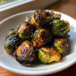 Close-up of roasted Brussels sprouts coated in a dark, shiny Sticky Brussels Sprouts Glaze in a white bowl.