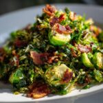 A mound of Sautéed Shredded Brussels Sprouts mixed with crispy bacon pieces served on a white plate.