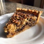 A close-up slice of rich texas trash pie featuring a gooey filling, pecans, and chocolate chips on a white plate.