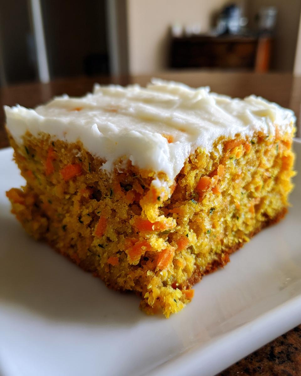 A close-up of a moist slice of Zucchini Carrot Bars recipe topped with thick white cream cheese frosting.