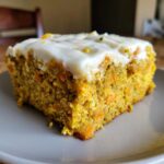 A close-up of a moist slice of Zucchini Carrot Bars topped with thick white cream cheese frosting.